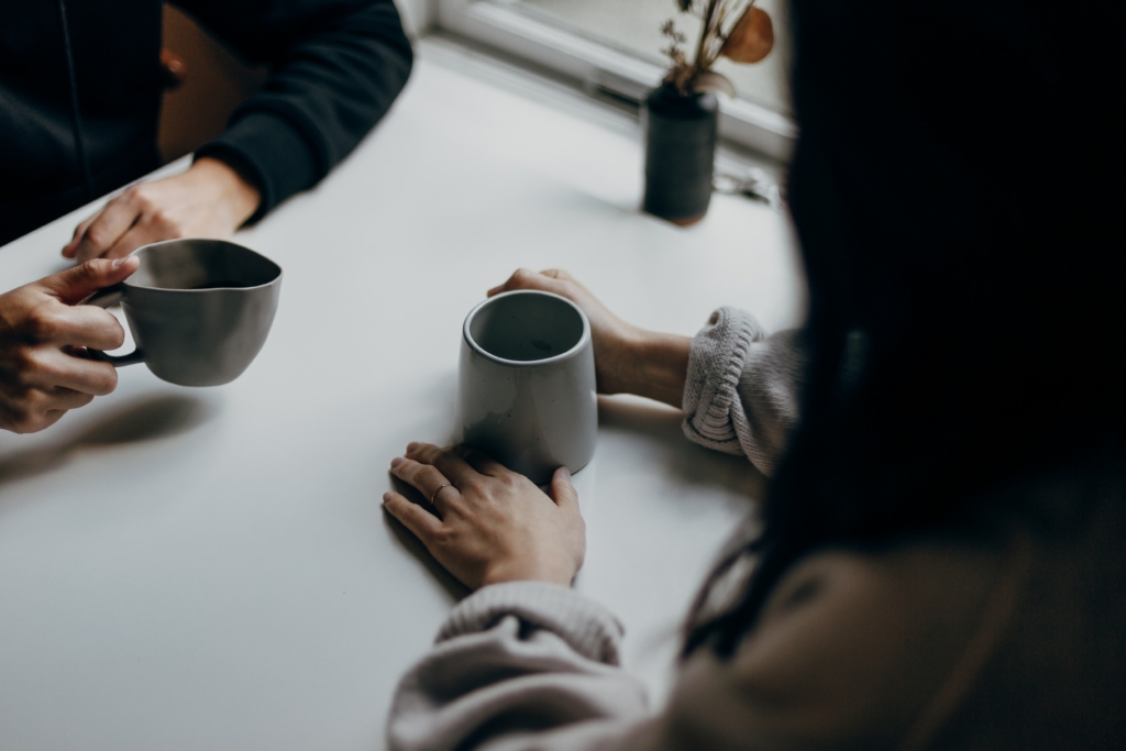 Two coffee cups on a table, each being held by a person out of shot. They are having a conversation.