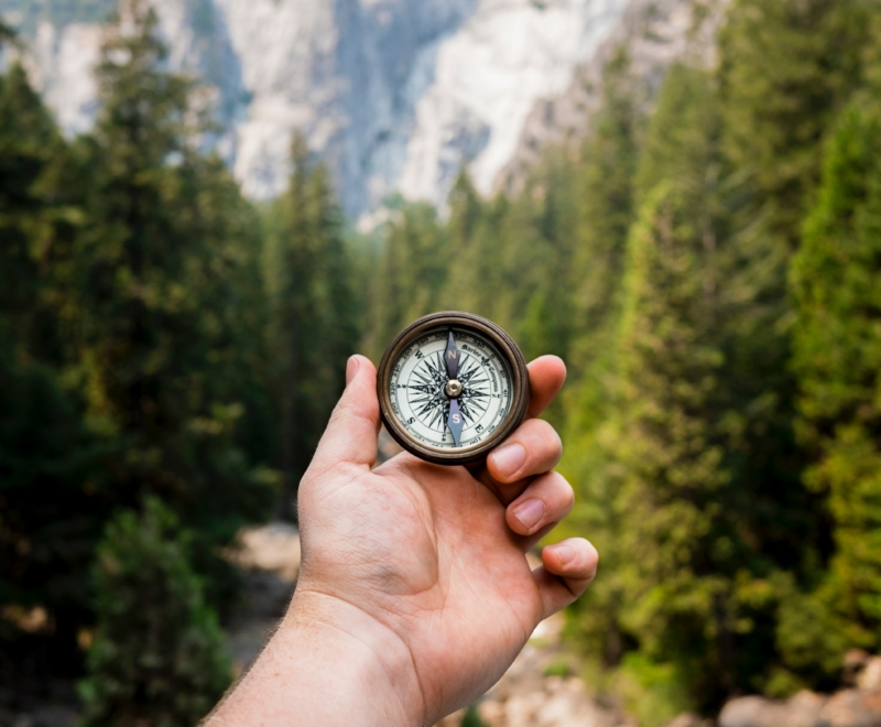 A hand holding a vintage compass in front of a mountain.